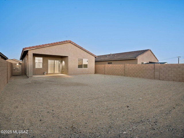 rear view of house with a patio, stucco siding, a fenced backyard, and a tiled roof