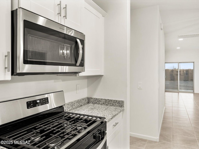 kitchen featuring light stone counters, light tile patterned floors, appliances with stainless steel finishes, white cabinets, and baseboards