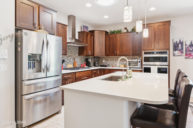 kitchen with sink, a center island with sink, wall chimney range hood, and appliances with stainless steel finishes