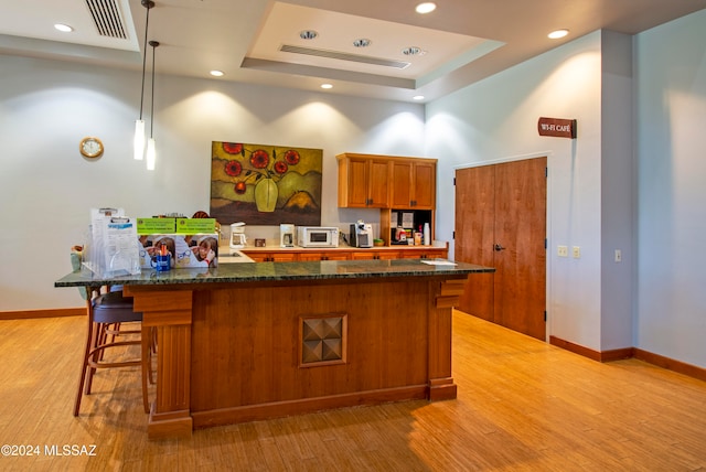 kitchen featuring hanging light fixtures, a high ceiling, dark stone counters, light hardwood / wood-style floors, and a tray ceiling