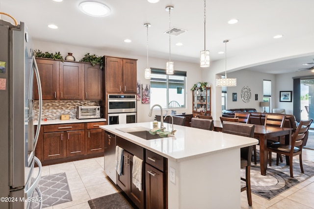 kitchen featuring appliances with stainless steel finishes, backsplash, sink, hanging light fixtures, and an island with sink