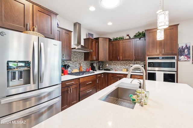 kitchen with decorative backsplash, wall chimney exhaust hood, stainless steel appliances, sink, and hanging light fixtures