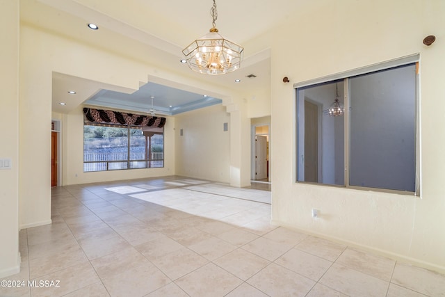 tiled spare room featuring a raised ceiling and a notable chandelier