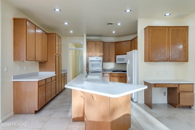 kitchen with sink, an island with sink, white appliances, a breakfast bar area, and light tile patterned flooring