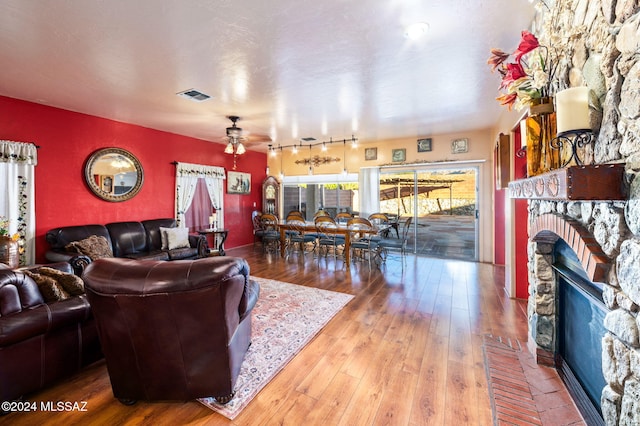 living room with a stone fireplace, ceiling fan, and hardwood / wood-style flooring