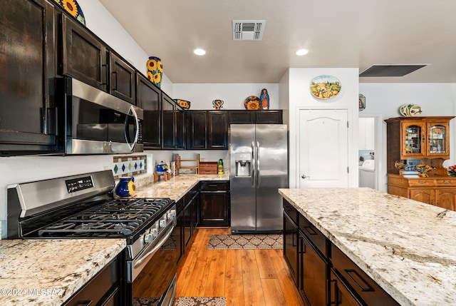 kitchen with light stone countertops, stainless steel appliances, light hardwood / wood-style flooring, washer / clothes dryer, and dark brown cabinets