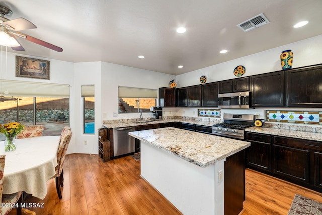 kitchen with light wood-type flooring, a center island, stainless steel appliances, and light stone counters