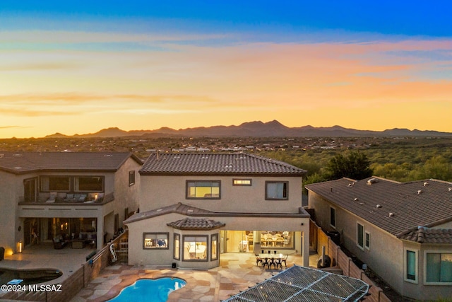 back house at dusk featuring a mountain view and a patio