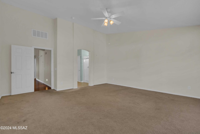 empty room with a high ceiling, carpet, and ceiling fan