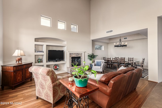 living room with light hardwood / wood-style floors, a fireplace, an inviting chandelier, and a high ceiling