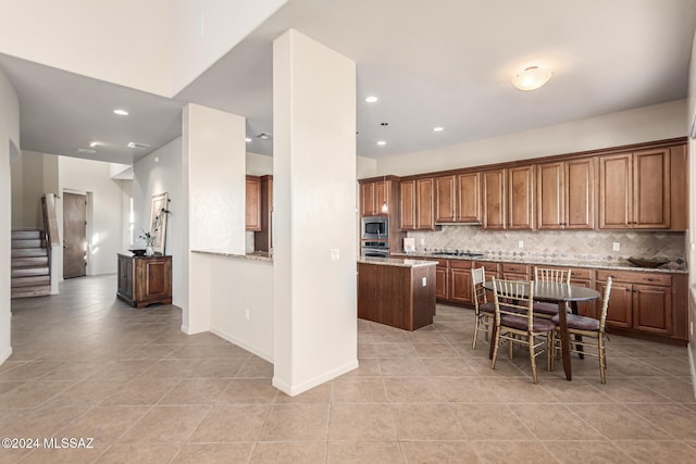 kitchen featuring light stone counters, backsplash, appliances with stainless steel finishes, light tile patterned flooring, and a center island