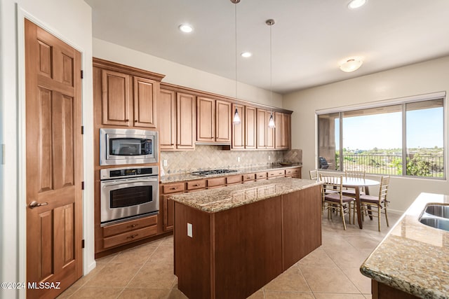 kitchen featuring stainless steel appliances, a kitchen island, light stone counters, and pendant lighting