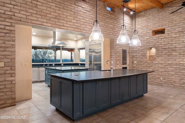 kitchen featuring a kitchen island with sink, hanging light fixtures, stainless steel refrigerator with ice dispenser, brick wall, and sink