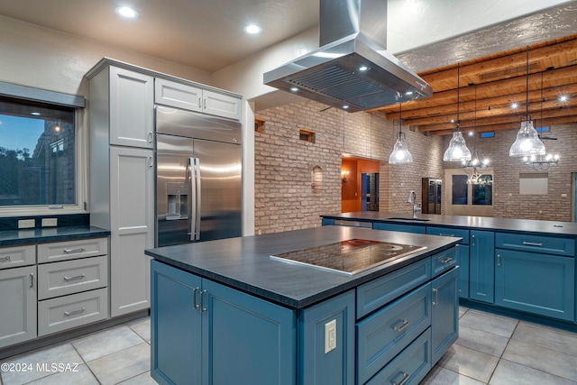 kitchen featuring island exhaust hood, beam ceiling, black electric cooktop, blue cabinets, and brick wall