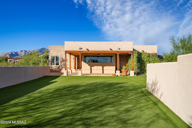 rear view of house with a patio area, a mountain view, a lawn, and ceiling fan