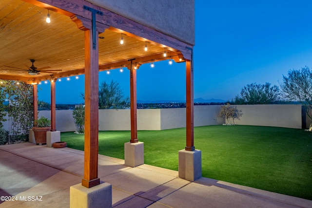 patio terrace at dusk featuring a lawn and ceiling fan