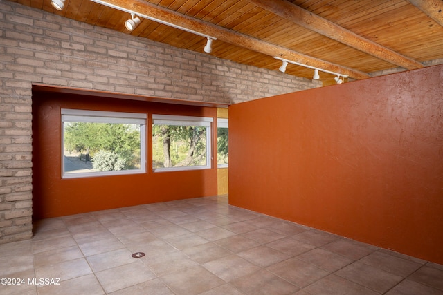 tiled empty room featuring wooden ceiling, beamed ceiling, brick wall, and rail lighting