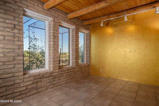 empty room with beam ceiling, brick wall, light tile patterned floors, and wood ceiling