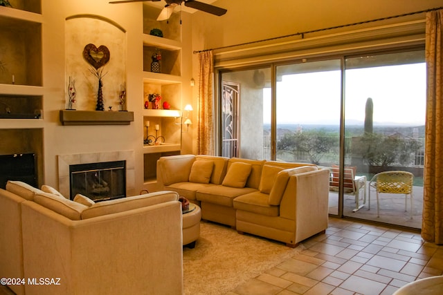 living room featuring built in features, a tiled fireplace, and ceiling fan