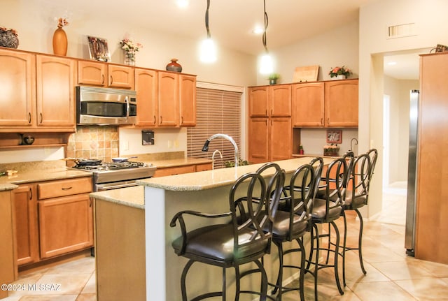 kitchen with stainless steel appliances, light stone counters, a center island with sink, a breakfast bar area, and light tile patterned flooring