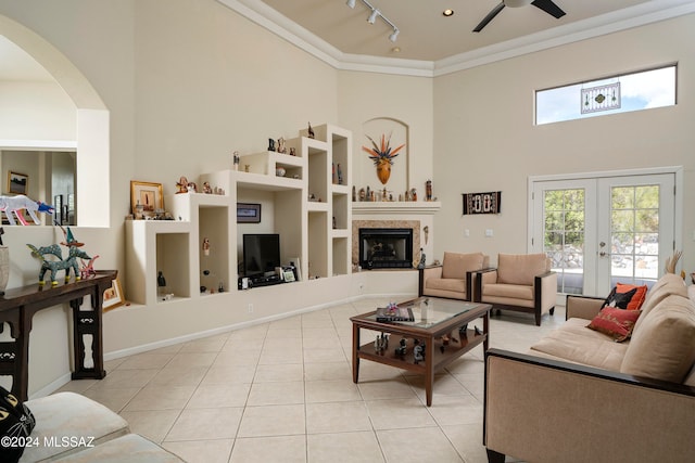 tiled living room featuring ceiling fan, french doors, rail lighting, a towering ceiling, and ornamental molding