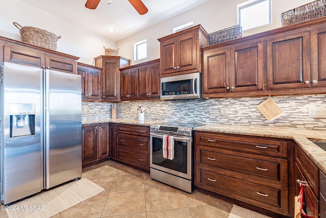 kitchen with decorative backsplash, ceiling fan, appliances with stainless steel finishes, light stone countertops, and light tile patterned flooring