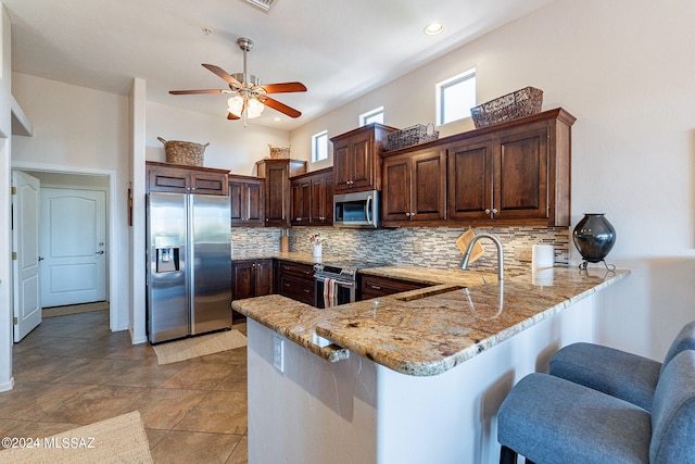 kitchen featuring tasteful backsplash, appliances with stainless steel finishes, sink, a kitchen bar, and kitchen peninsula