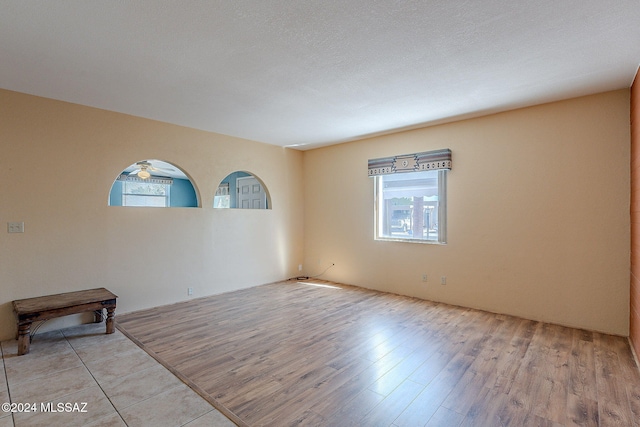 unfurnished room with ceiling fan, a textured ceiling, and light wood-type flooring