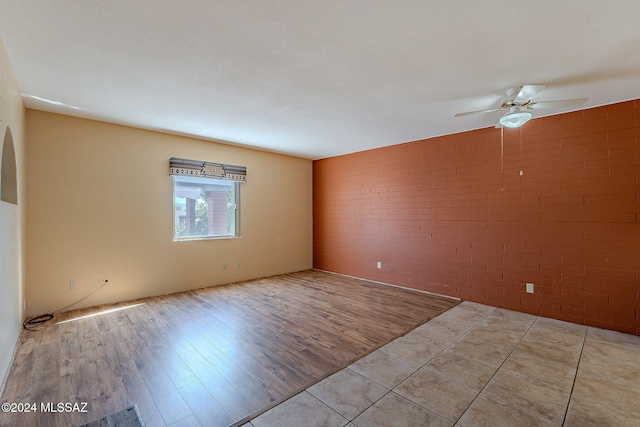 unfurnished room featuring ceiling fan, brick wall, and light wood-type flooring