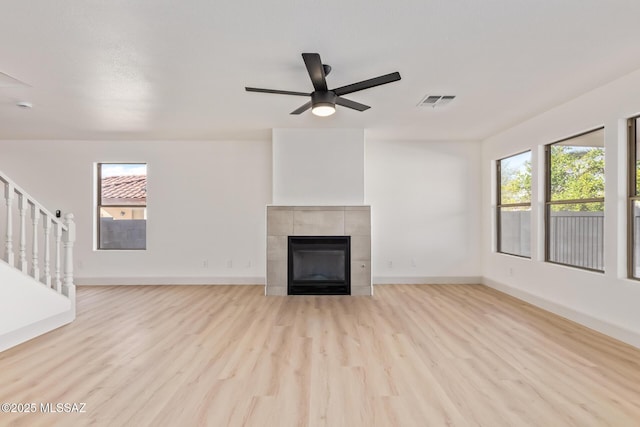 unfurnished living room with ceiling fan, light hardwood / wood-style flooring, a tile fireplace, and a wealth of natural light