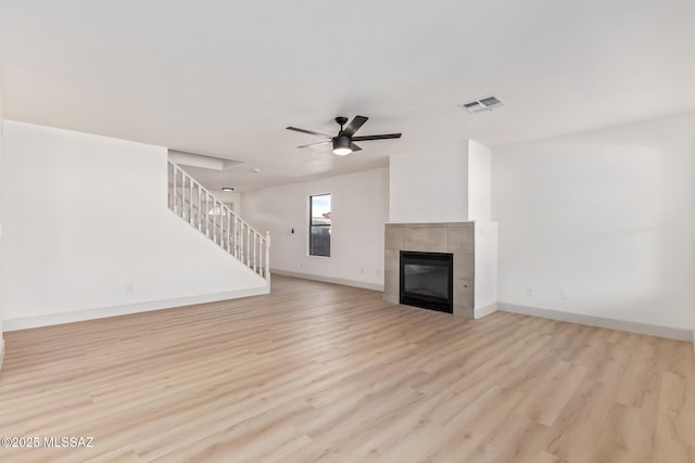 unfurnished living room with light hardwood / wood-style flooring, a tile fireplace, and ceiling fan