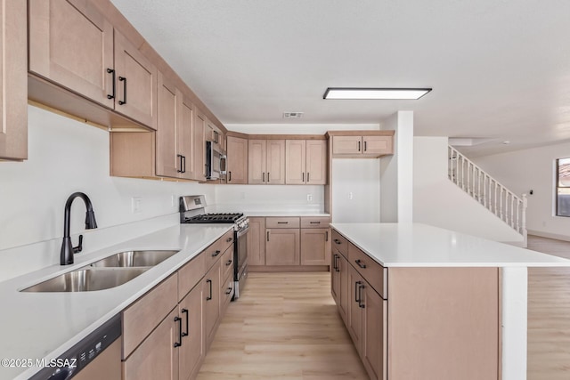 kitchen with a kitchen island, appliances with stainless steel finishes, sink, and light hardwood / wood-style flooring