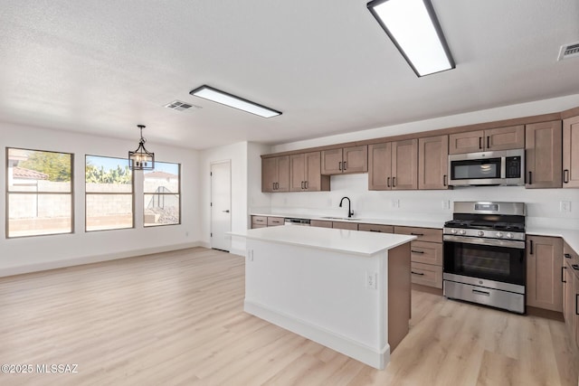 kitchen featuring appliances with stainless steel finishes, pendant lighting, sink, a center island, and light hardwood / wood-style floors