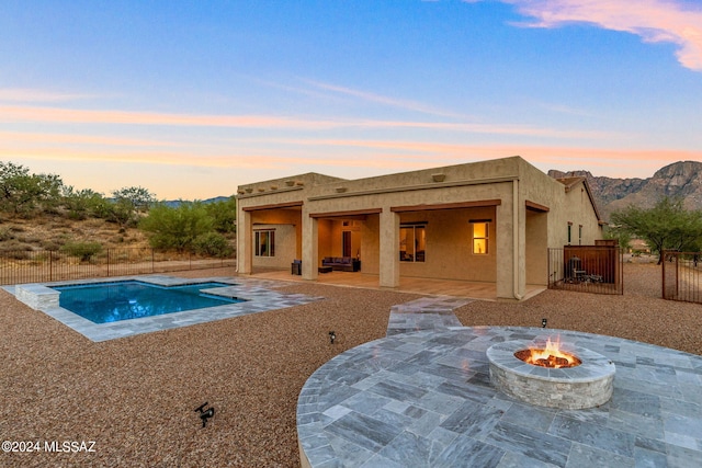 pool at dusk with a mountain view, a patio area, and an outdoor fire pit