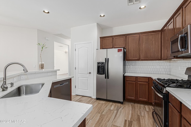 kitchen featuring backsplash, sink, appliances with stainless steel finishes, light hardwood / wood-style floors, and light stone counters