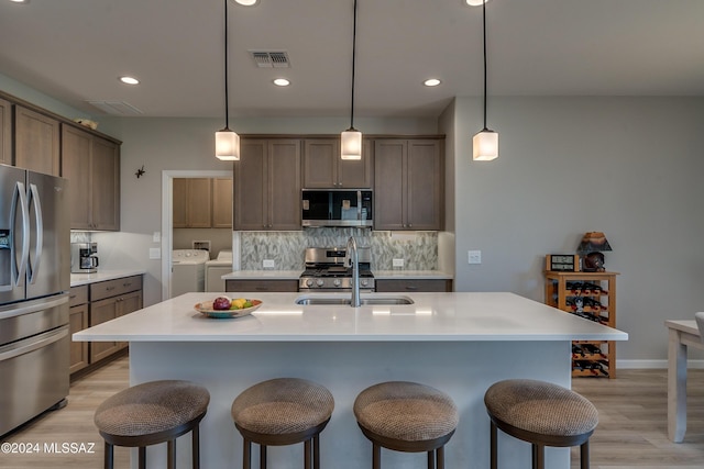 kitchen with washer and clothes dryer, pendant lighting, an island with sink, and appliances with stainless steel finishes