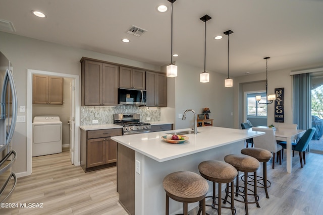 kitchen featuring sink, hanging light fixtures, light hardwood / wood-style flooring, washer / clothes dryer, and appliances with stainless steel finishes