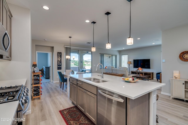 kitchen featuring appliances with stainless steel finishes, light wood-type flooring, sink, hanging light fixtures, and an island with sink