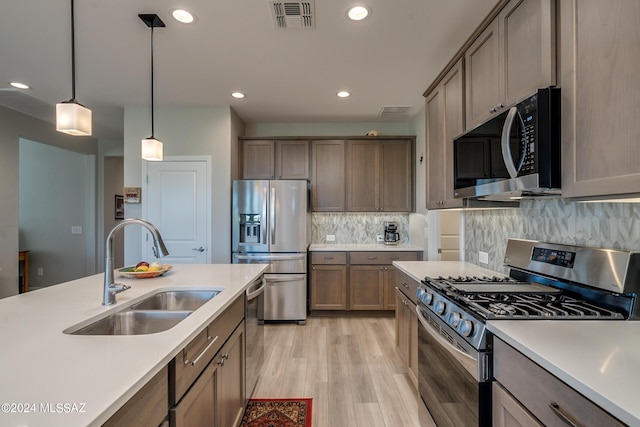 kitchen featuring pendant lighting, backsplash, sink, light hardwood / wood-style flooring, and appliances with stainless steel finishes