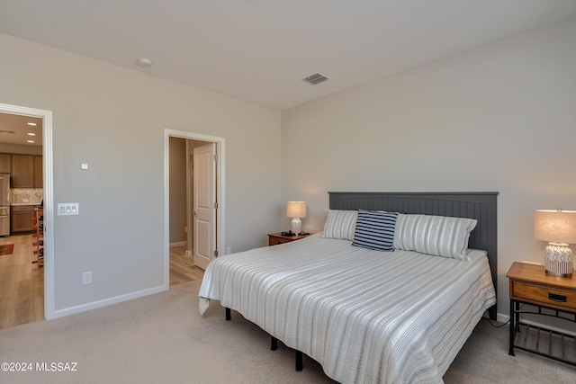 bedroom with light colored carpet, stainless steel refrigerator, and ensuite bath