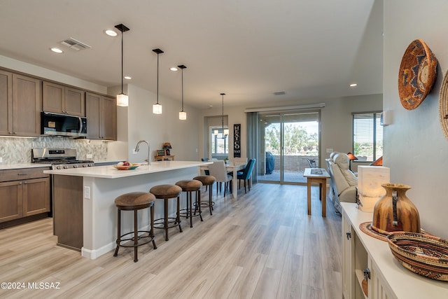 kitchen with hanging light fixtures, backsplash, a center island with sink, appliances with stainless steel finishes, and light wood-type flooring