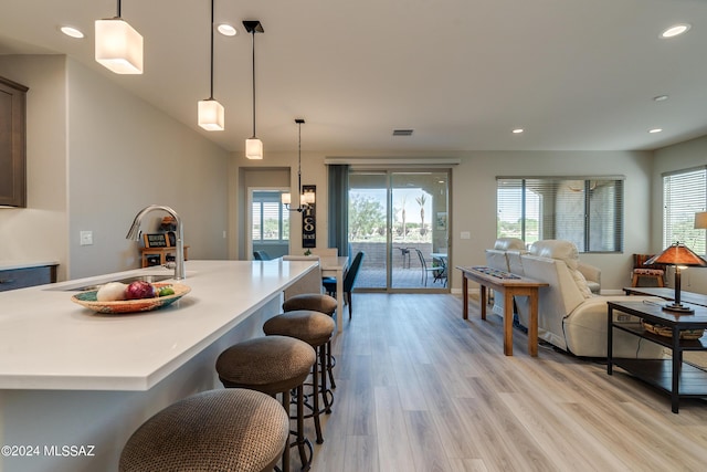 kitchen with pendant lighting, light wood-type flooring, sink, and a kitchen island with sink