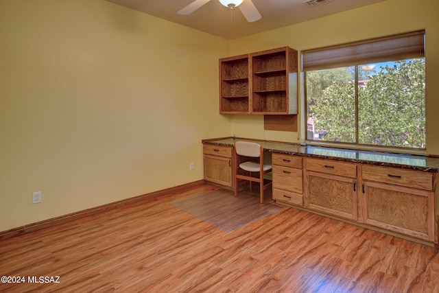 unfurnished office featuring built in desk, ceiling fan, and light hardwood / wood-style flooring