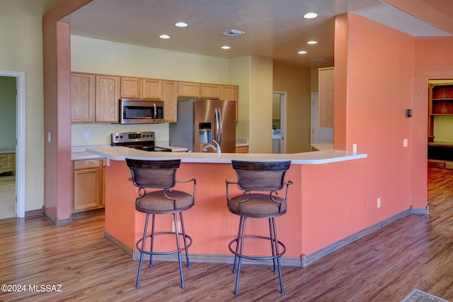 kitchen with a kitchen breakfast bar, kitchen peninsula, stainless steel appliances, and light wood-type flooring