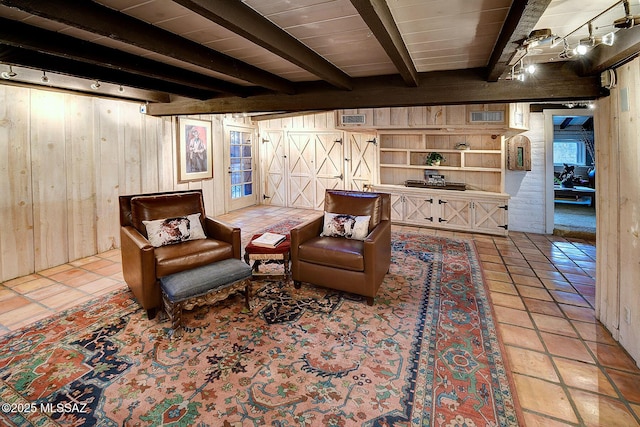 living area featuring beamed ceiling, track lighting, light tile patterned floors, and wood walls