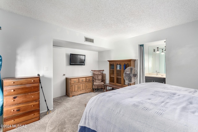 bedroom with a chandelier, a textured ceiling, light colored carpet, and ensuite bath