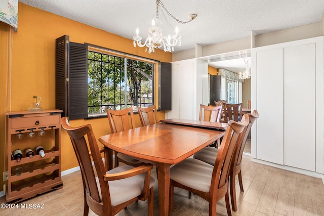 dining space with light hardwood / wood-style floors, an inviting chandelier, and a textured ceiling