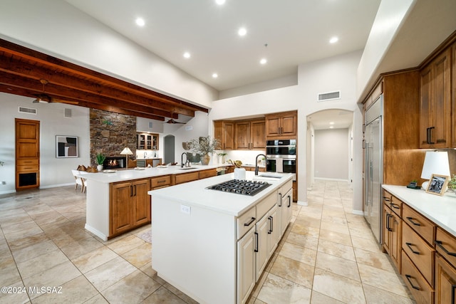 kitchen with a stone fireplace, sink, an island with sink, appliances with stainless steel finishes, and kitchen peninsula