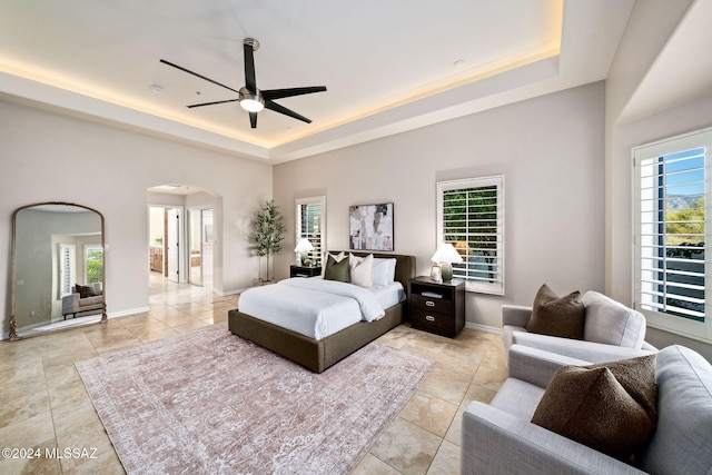 bedroom featuring a raised ceiling, multiple windows, and ceiling fan