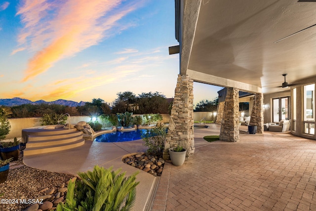 patio terrace at dusk featuring a mountain view, a swimming pool with hot tub, and ceiling fan